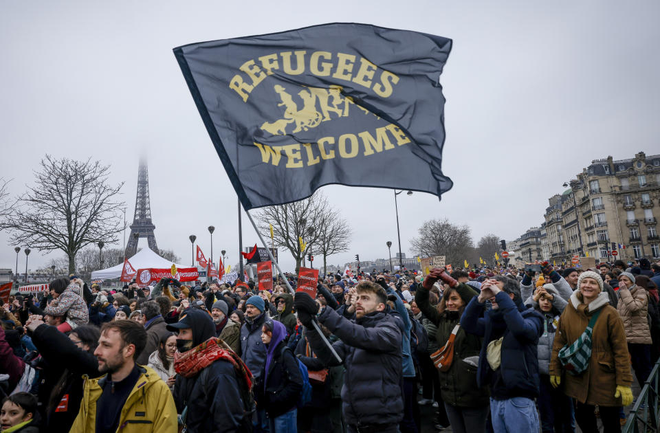 An opponent of France's immigration law holds a flag during a protest in Paris, Sunday, Jan. 21, 2024. The Constitutional Council is reviewing next week the government's controversial immigration law , to check that measures is in line with the Constitution. Eiffel Tower in the background. (AP Photo/Thomas Padilla)