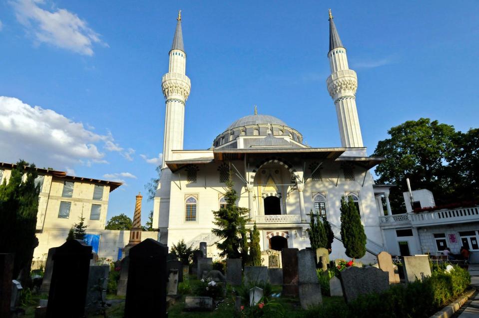 Açık mavi gökyüzüne karşı, ortasında kubbe bulunan iki yüksek minareli, fildişi renginde bir bina.