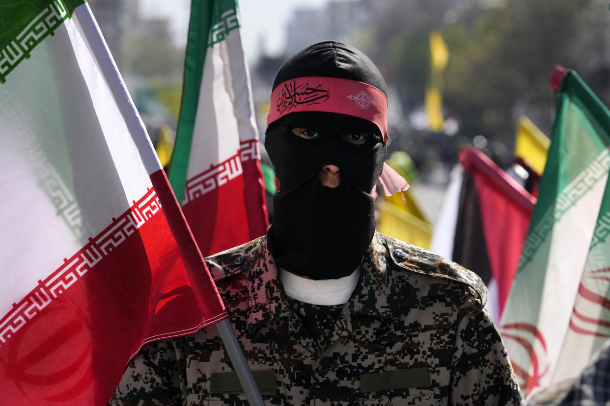 A member of the Iranian paramilitary Basij force holds an Iranian flag as he covers her face in the Palestinian and Lebanese militants style in an annual rally to mark Quds Day, or Jerusalem Day, to support the Palestinians in Tehran, Iran, Friday, April 5, 2024. In the rally in Tehran, thousands attended a funeral procession for the seven Revolutionary Guard members killed in an airstrike widely attributed to Israel that destroyed Iran's Consulate in the Syrian capital on Monday. (AP Photo/Vahid Salemi)