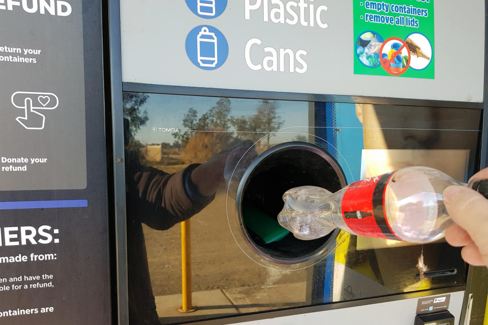 A hand drops a bottle into a chute at a NSW Government Return and Earn centre. Source: Getty Images