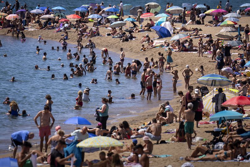 Bañistas se refrescan en el agua mientras otros toman el sol en una playa de Barcelona.