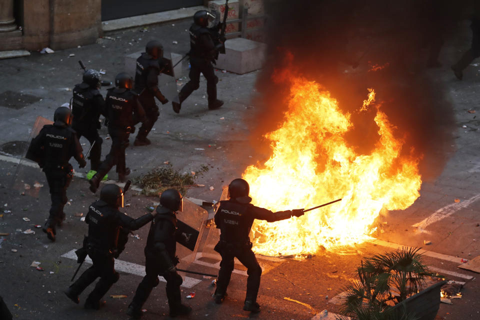 Police officers run past a burning barricade on the fifth day of protests over the conviction of a dozen Catalan independence leaders in Barcelona, Spain, Friday, Oct. 18, 2019. Tens of thousands of flag-waving demonstrators demanding Catalonia's independence and the release from prison of their separatist leaders have flooded downtown Barcelona. The protesters have poured into the city after some of them walked for three days in "Freedom marches" from towns across the northeastern Spanish region, joining students and workers who have also taken to the streets on a general strike day. (AP Photo/Manu Fernandez)