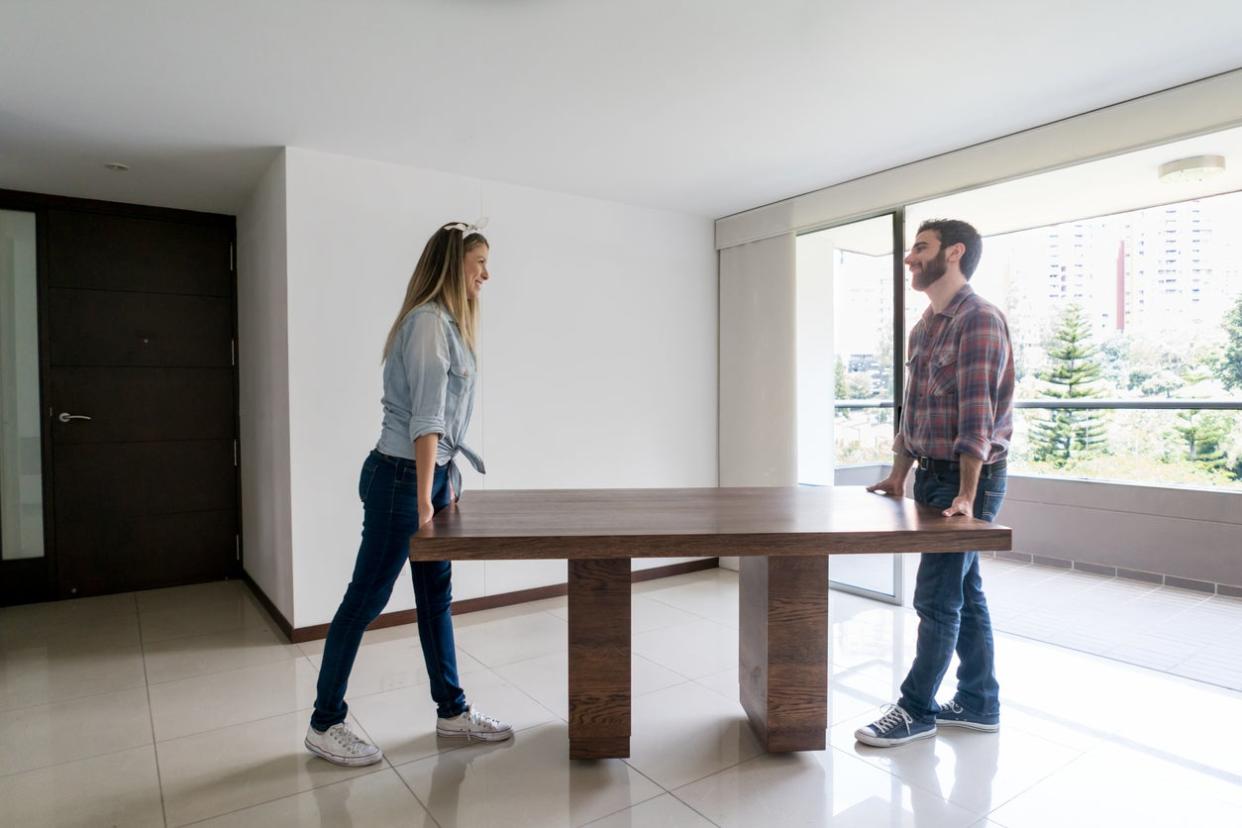 Young couple moving into their new place carrying a dining table while talking and having fun