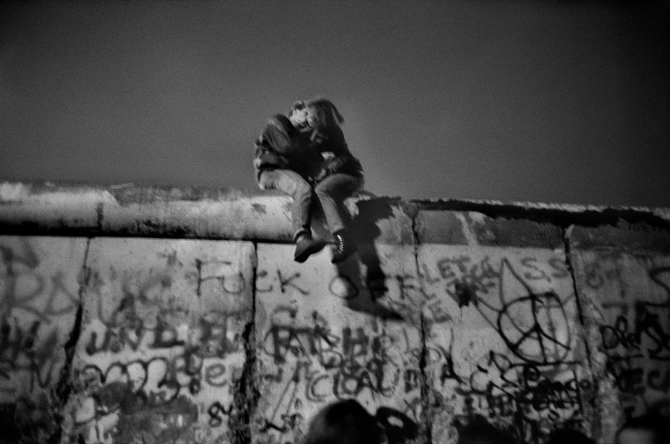 <p>Berlin Wall, Sunday, Dec. 31, 1989. “A few days after the fall of the Berlin Wall (the 9th of November, 1989), joy and enthusiasm were continuous. The euphoria grew even greater on New Year’s Eve. A very dense human tide had gathered around the Brandenburg Gate: warmth, embraces here and there … In this incessant frenzy, tears blended with laughter. People of all ages, backgrounds and nationalities were becoming closer as the fireworks and squibs exploded relentlessly. Champagne was flowing.<br> After photographing the jubilation of this overexcited crowd, I decided to move to a quiet place. I glimpsed, hidden by a row of shrubs, a young couple sitting astride the top of the wall. They were surrendering to this intimate and peaceful moment to love each other and celebrate this new freedom.” (© Guy Le Querrec/Magnum Photos) </p>