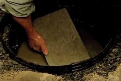 Hand places flat stone in basin.