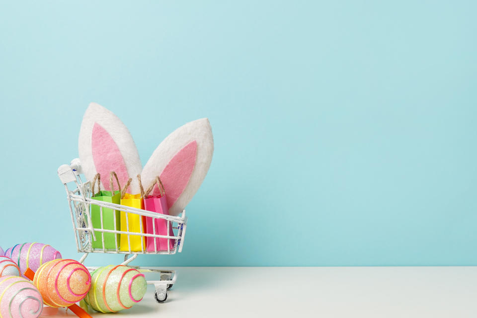 Colorful painted Easter egg with shopping cart, bunny ears and paper bags , blue background, copy space