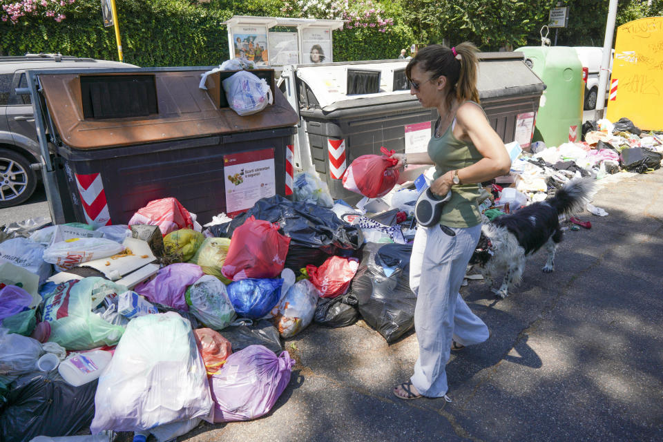 In this photo taken on Monday, June 24, 2019, a woman walks by uncollected garbage, in Rome. Doctors in Rome are warning of possible health hazards caused by overflowing trash bins in the city streets, as the Italian capital struggles with a renewed garbage emergency aggravated by the summer heat.(AP Photo/Andrew Medichini)