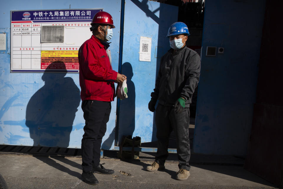 Workers wearing face masks to protect against the coronavirus stand outside of a construction site in Beijing, Thursday, Oct. 22, 2020. The number of confirmed COVID-19 cases across the planet has surpassed 40 million, but experts say that is only the tip of the iceberg when it comes to the true impact of the pandemic that has upended life and work around the world. (AP Photo/Mark Schiefelbein)