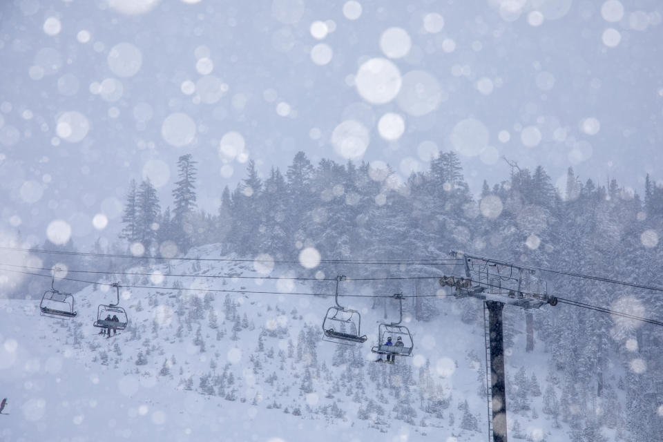 In this photo provided by Mammoth Lakes Tourism, snow falls as skiers ride a lift in Mammoth Lakes, Calif., Tuesday, Dec. 19, 2023. A foot of snow has fallen at the resort and all base areas are open. Forecasters are warning of potential flooding from excessive rainfall as a slow-moving Pacific storm blows into California. (Samantha Lindberg/Mammoth Lakes Tourism via AP)