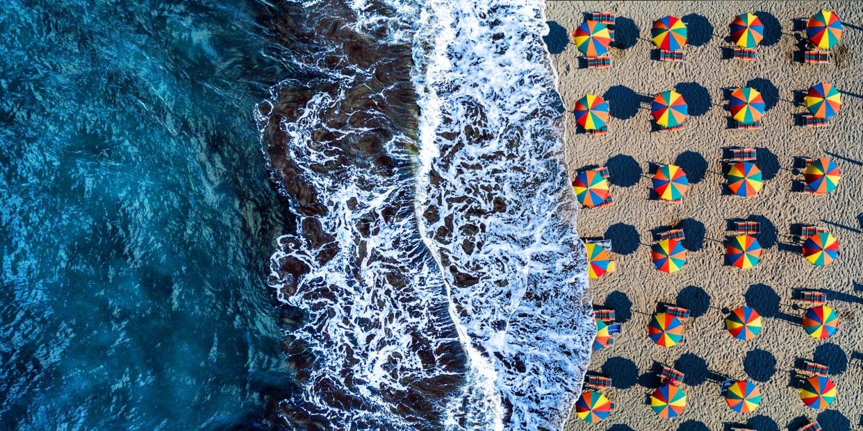 photo composite of aerial view of waves crashing onto a shore crowded with colorful umbrellas