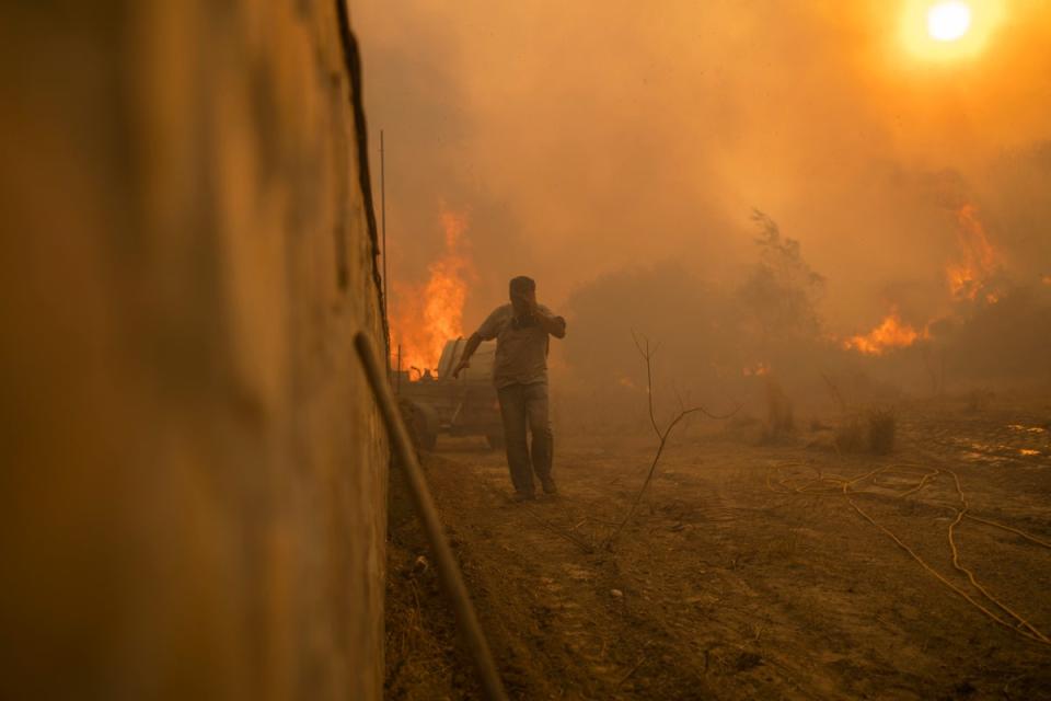 A person runs to avoid the flames of a wildfire in Gennadi village, on the Aegean Sea island of Rhodes, in the summer (Copyright 2023 The Associated Press. All rights reserved)