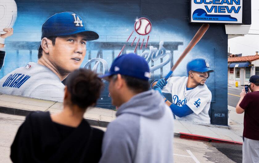 HERMOSA BEACH-CA-DECEMBER 19, 2023: People stop to take photos of a mural featuring newest Dodger player Shohei Ohtani, left, and Mookie Betts, right, by artist Gustavo Zermeno, Jr. on the side wall of Ocean View Liquor store in Hermosa Beach on Tuesday, December 19, 2023. (Christina House / Los Angeles Times)