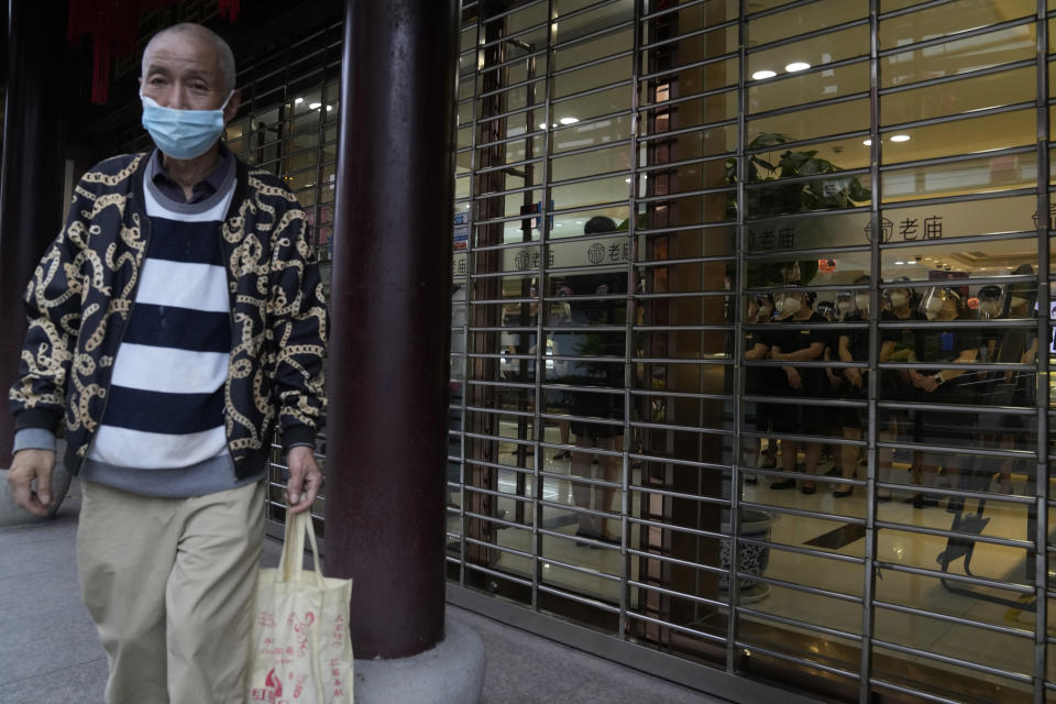 A man waits to enter a mall as workers wearing masks receive their briefing before starting work, Thursday, June 2, 2022, in Shanghai. Traffic, pedestrians and joggers reappeared on the streets of Shanghai on Wednesday as China's largest city began returning to normalcy amid the easing of a strict two-month COVID-19 lockdown that has drawn unusual protests over its heavy-handed implementation. (AP Photo/Ng Han Guan)