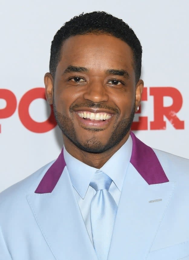 Larenz in a light blue suit with purple collar detail posing at a media event