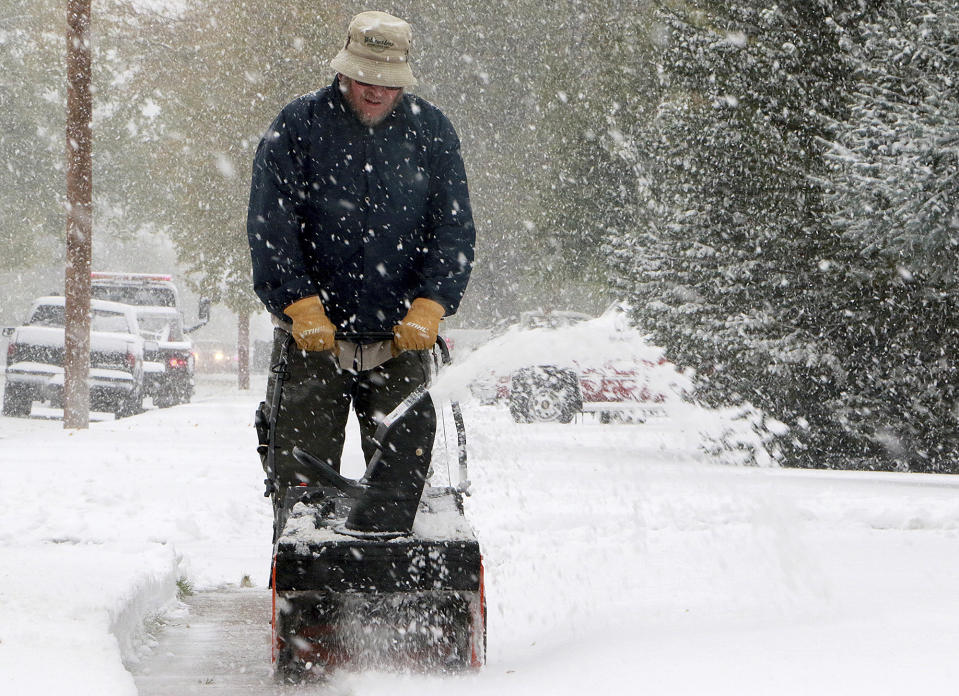 Kevin Hill uses a snow blower to remove snow from his front sidewalk as snow continues to fall Thursday, Oct. 10, 2019, in Scottsbluff, Neb. The Panhandle saw its first snow of the season Wednesday night into Thursday. (Lauren Brant/The Star-Herald via AP)