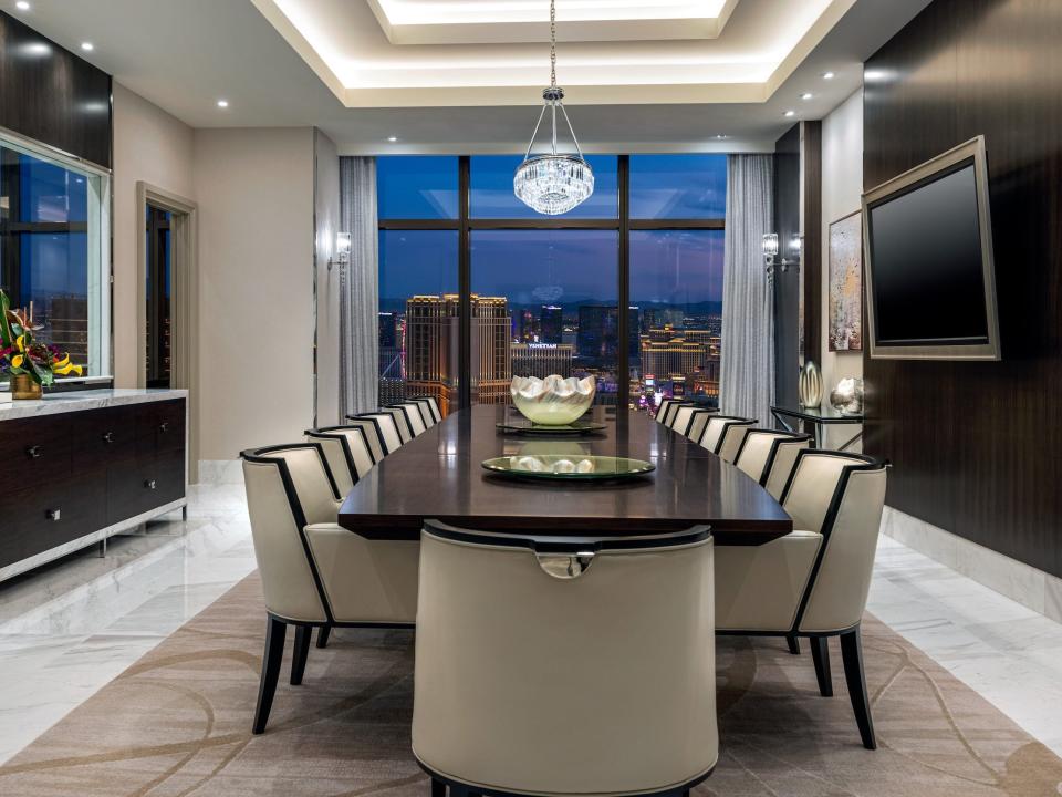 a long multi-person dining room with a TV  next to a large floor to ceiling window with views of Las Vegas