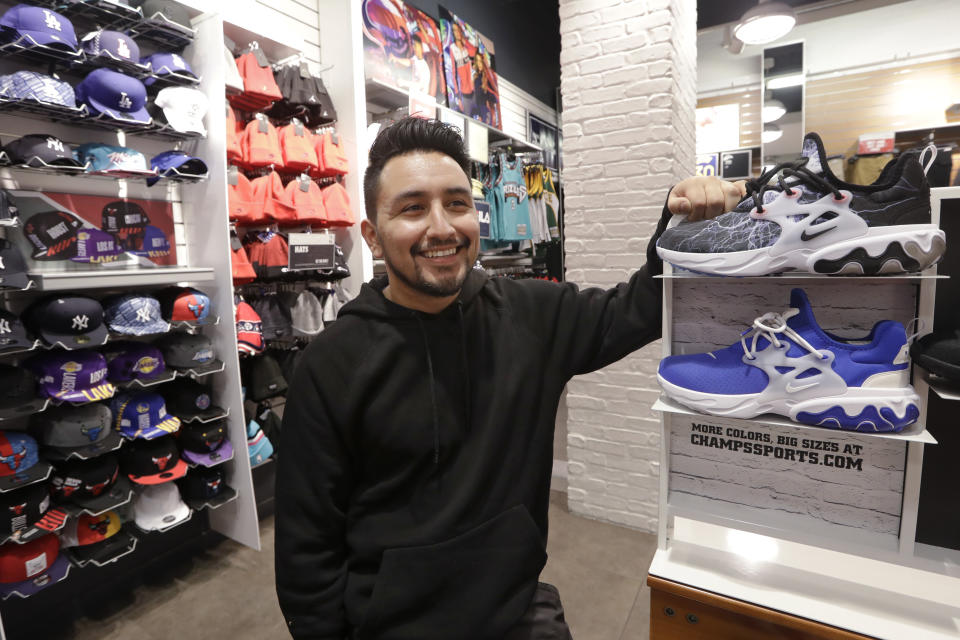 Victor Duran, a co-manager of a sports apparel store at the Southcenter mall, south of Seattle, poses for a photo at the store, Wednesday, Dec. 11, 2019, in Tukwila, Wash. Duran, 23, said he makes about $52,000 a year and doesn't get overtime, but is required to work at least 45 hours per week, and up to 60 during the holidays. Duran is one employee who could benefit from new overtime rules in Washington state, which will allow hundreds of thousands of workers who have been exempt to begin collecting when they work more than 40 hours per week. (AP Photo/Elaine Thompson)