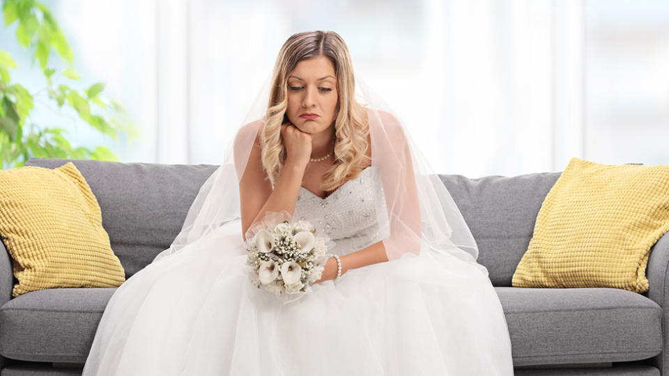 Upset bride sits on couch in her wedding dress