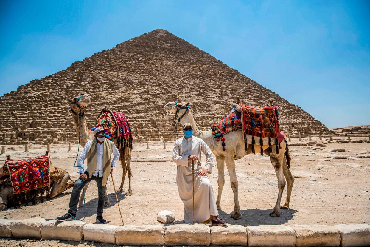 Mask-clad camel guides stand by their camels near the Great Pyramid of Khufu (Cheops) at the Giza Pyramids necropolis on the southwestern outskirts of Cairo on July 1, 2020 as the archaeological site reopens. While cafes and shops have also reopened, public beaches and parks remain closed.