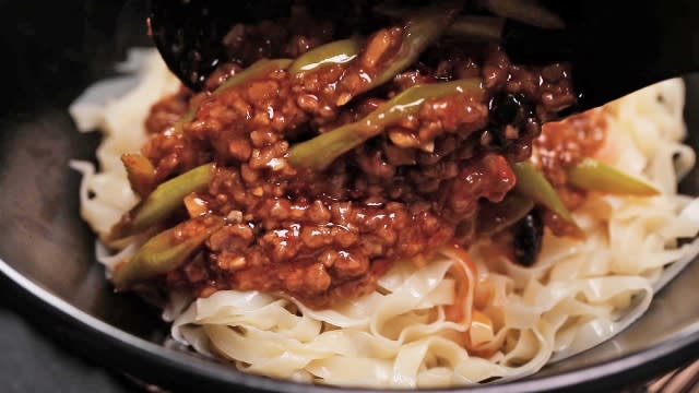 Scooping spicy bean paste sauce and minced beef onto meepok noodles