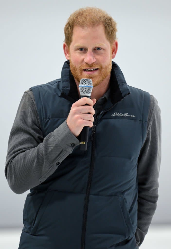 Prince Harry speaking into a microphone, wearing a casual zip-up vest