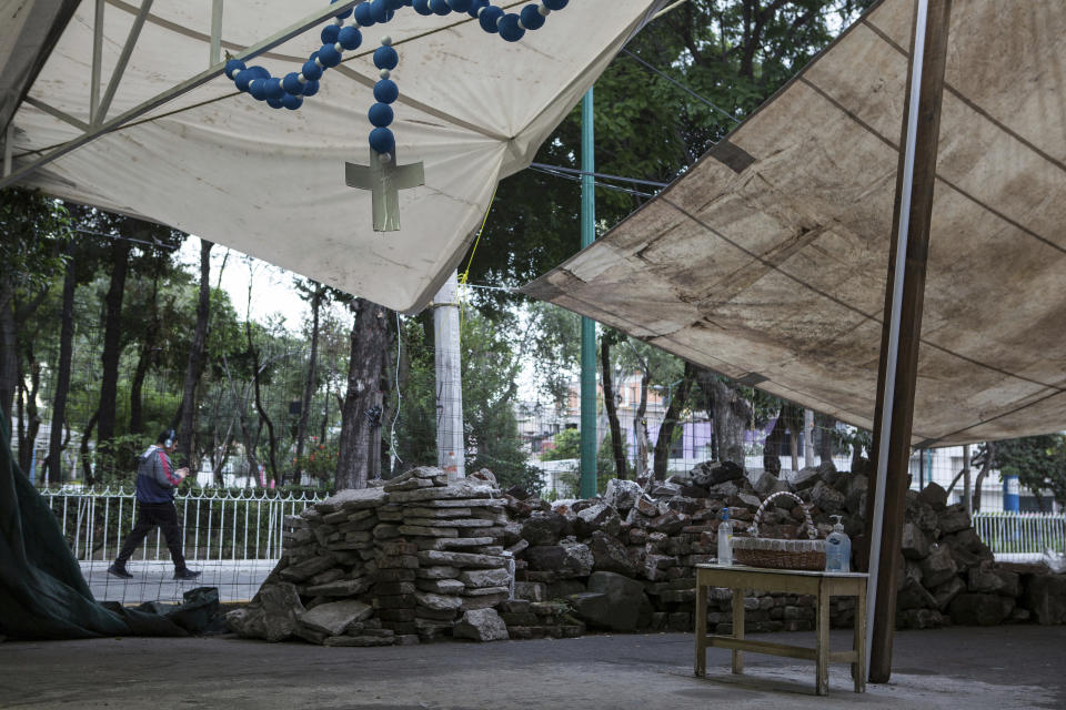 Debris caused by an earthquake five years ago sits stacked next to a table with a donations basket and bottles of antibacterial gel for parishioners arriving to an outdoor Mass held under a tent just outside Our Lady of the Angels Catholic church, as it undergoes restoration work, in the Guerrero neighborhood of Mexico City, Sunday, Aug. 7, 2022. (AP Photo/Ginnette Riquelme)