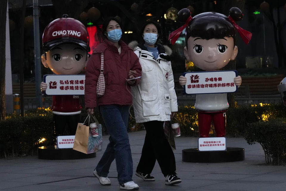 Women wearing masks walk past cartoon characters in Beijing, China, Tuesday, Dec. 28, 2021. Advertisements featuring some Chinese models have sparked feuding in China over whether their appearance and makeup are perpetuating harmful stereotypes of Asians. (AP Photo/Ng Han Guan)