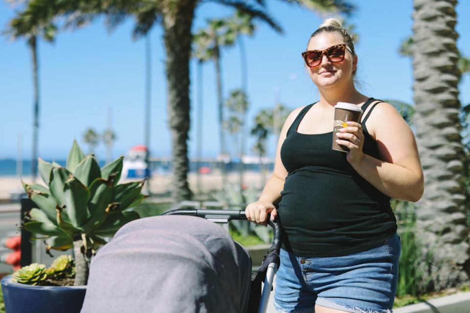 A woman in sunglasses pushing a stroller near the beach.