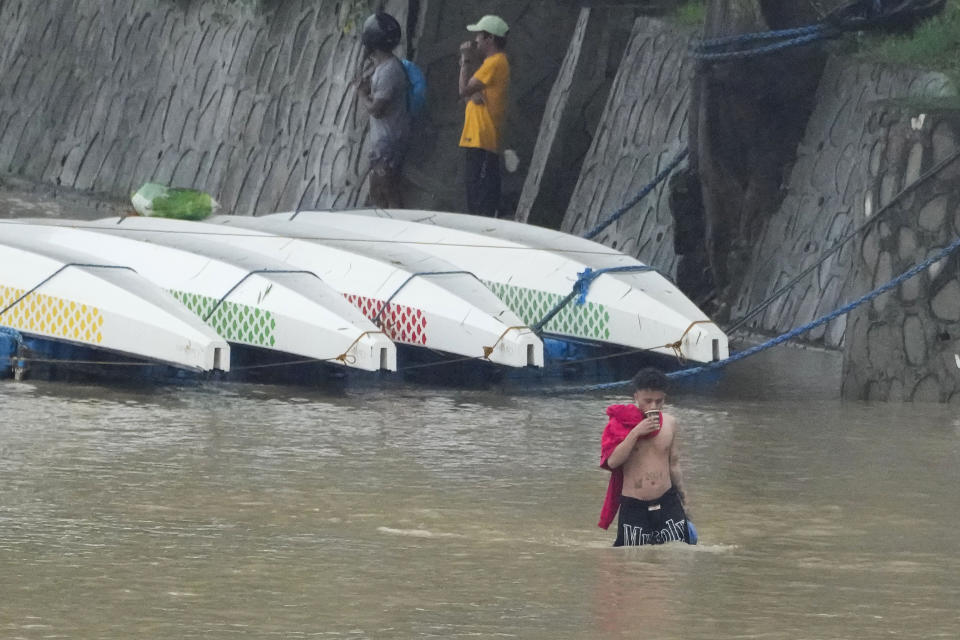 A man drinks coffee as he negotiates a swollen river due to enhanced rains brought about by Typhoon Doksuri on Thursday, July 27, 2023, in Marikina city, Philippines. Typhoon Doksuri lashed northern Philippine provinces with ferocious wind and rain Wednesday, leaving several people dead and displacing thousands of others as it blew roofs off houses, flooded low-lying villages and triggered dozens of landslides, officials said. (AP Photo/Aaron Favila)