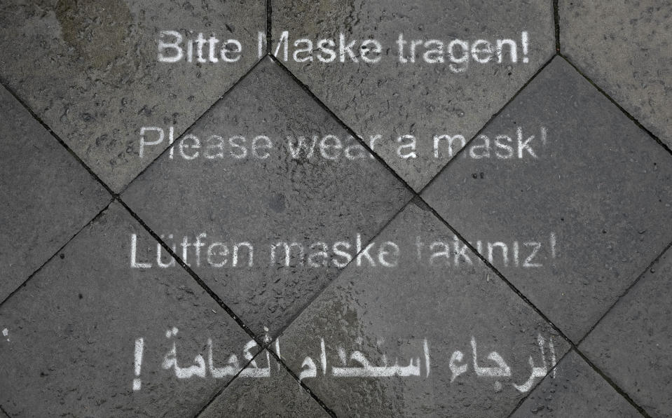 A notice in various languages to wear a face mask against a Corona Covid-19 infection is sprayed onto a sidewalk in Berlin, Germany, Tuesday, Jan. 4, 2022. (AP Photo/Michael Sohn)