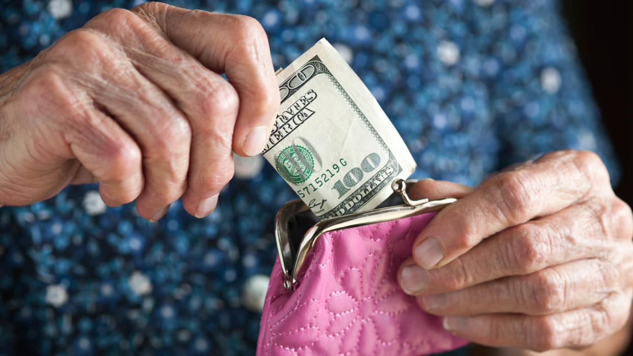 Senior Adult holding a one hundred dollar bill and a pink change purse.