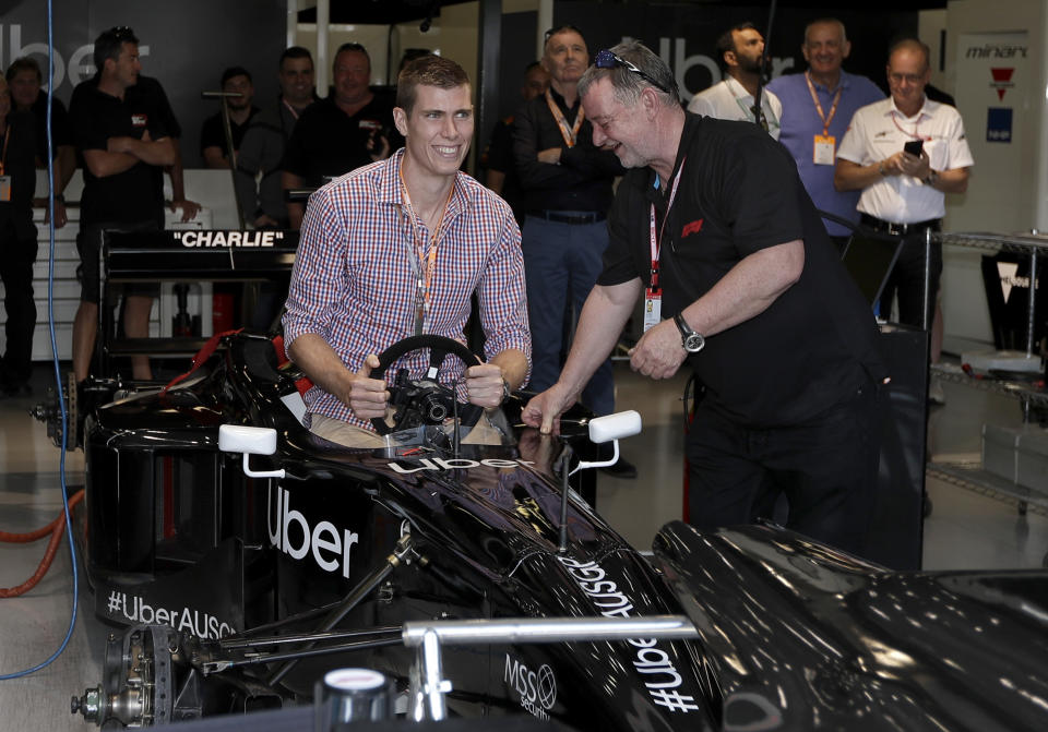 FILE - In this March 16, 2019, file photo Australian Rules Football player Mason Cox of the U.S., center, attempts to get into a 2-seat Formula One car while visiting the pit during a practice session for the Australian Grand Prix in Melbourne, Australia. Cox said a rude comment from an opposing fan about catching COVID-19 inspired him to kick three crucial goals in a row in his Collingwood Magpies' playoff win over the West Coast Eagles in the Aussie rules Australian Football League, Saturday, Oct. 3, 2020. (AP Photo/Rick Rycroft, File)