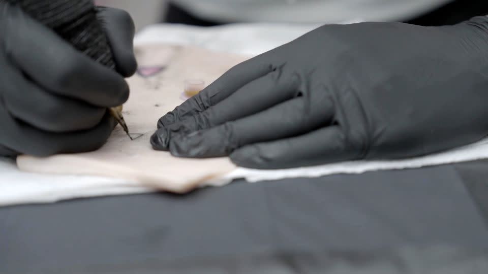 A tattoo artist in London practices with smart ink developed by researcher Ali Yetisen on a piece of pig skin. - CNN
