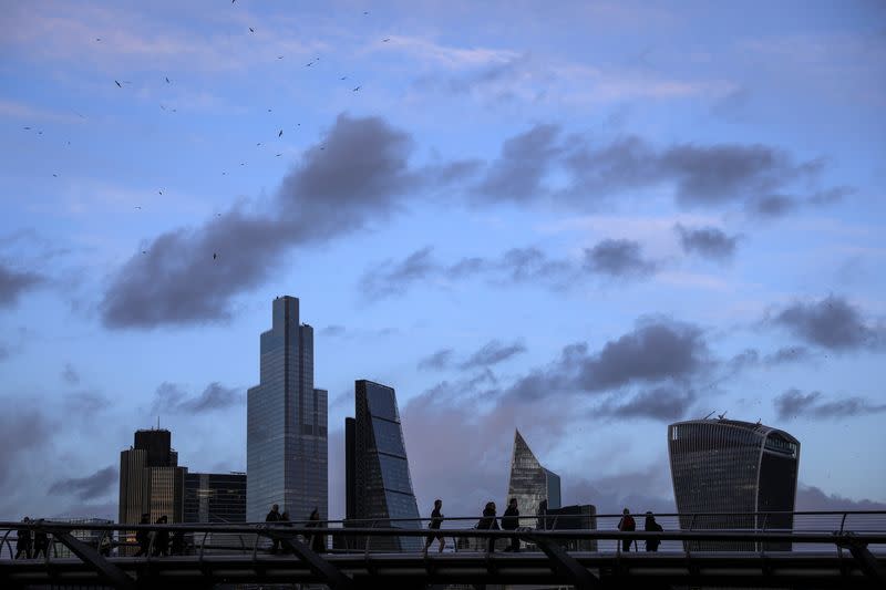 FILE PHOTO: Pedestrians walk over the Millennium Bridge in view of skyscrapers in the financial district in London