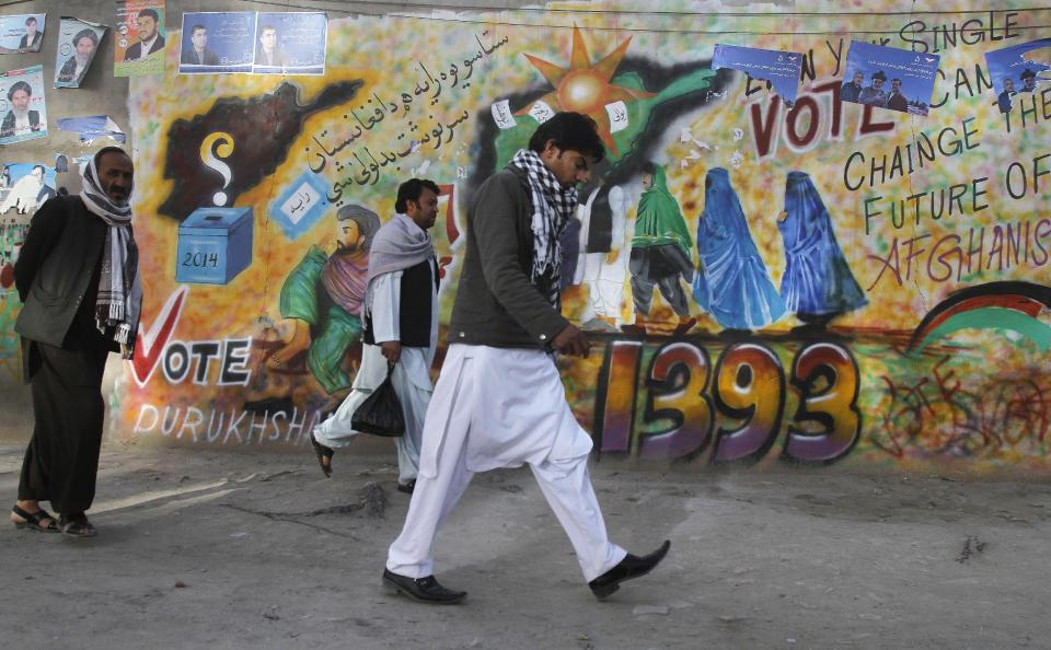 Afghan men walk passed an election graffiti poster urging people to go to the polls in Kandahar, southern Afghanistan, Wednesday, March 26, 2014. Eight Afghan presidential candidates are campaigning in the presidential election scheduled for April 5, 2014. (AP Photo/Allauddin Khan)