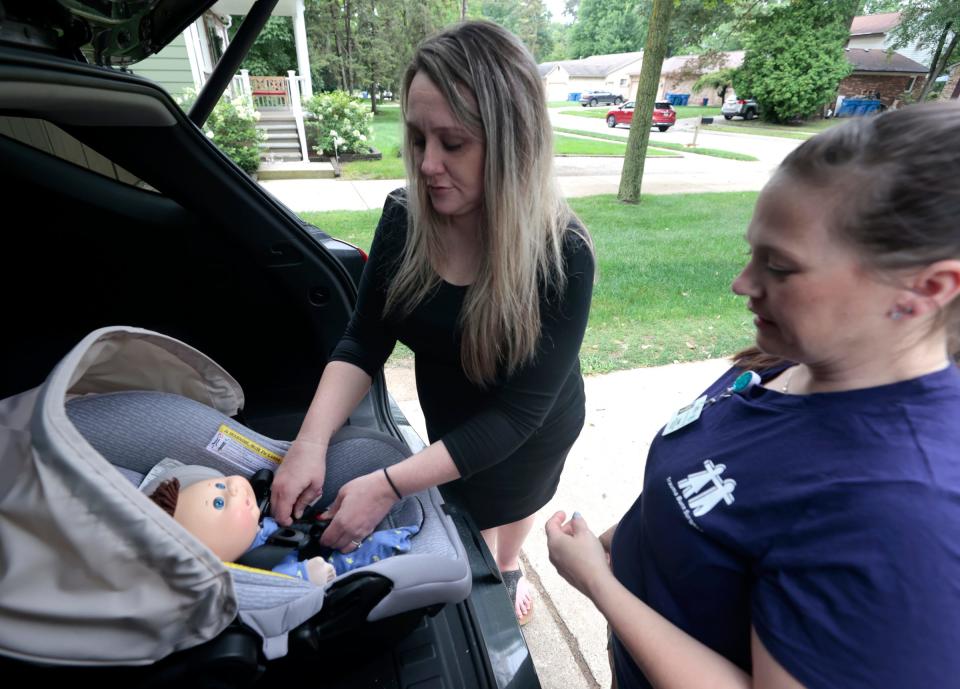 Jessica Henson, 33, of Warren, who is 32 weeks pregnant, works at buckling up a doll into an infant car seat as Renee Zarr, a child passenger safety technician and instructor at the Children's Hospital of Michigan, looks on at Henson's home on July 27, 2023.