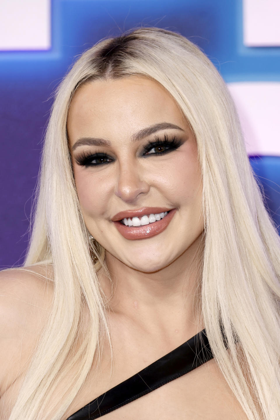 Tana Mongeau smiles for the camera in a one-shoulder dress and dramatic eye makeup.