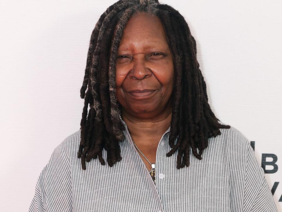 Whoopi Goldberg poses for photos in a striped shirt dress.