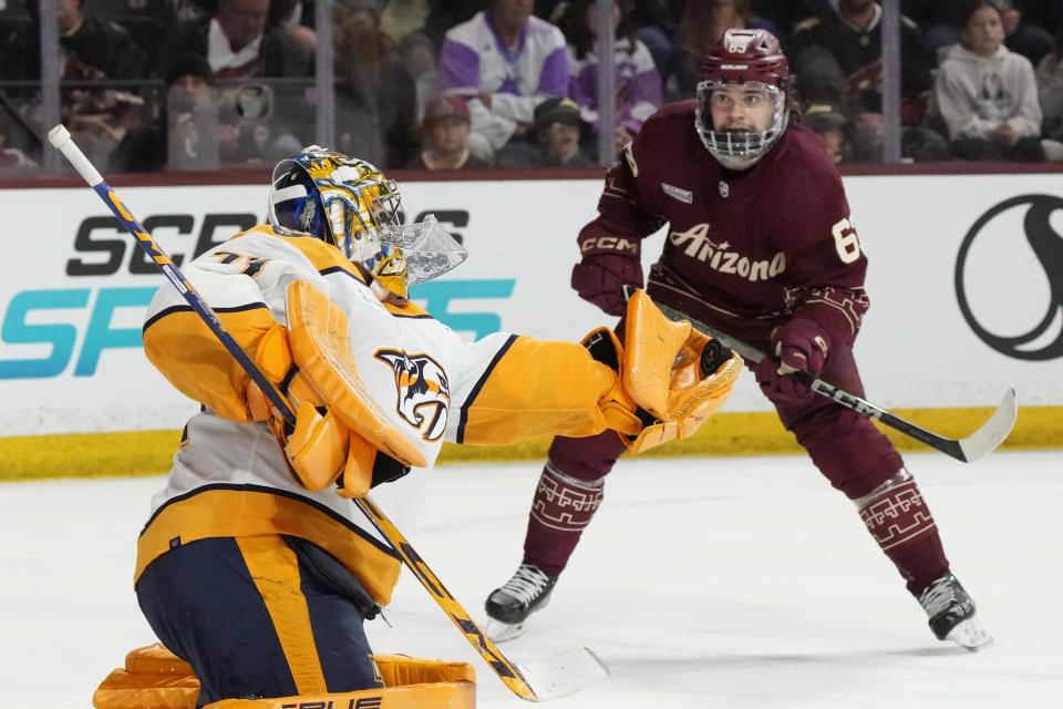 Nashville Predators goaltender Juuse Saros, left, makes a gloves save as Matias Maccelli, right, looks on during the third period of an NHL hockey game Saturday, Jan. 20, 2024, in Tempe, Ariz. The Coyotes won 3-2. (AP Photo/Ross D. Franklin)