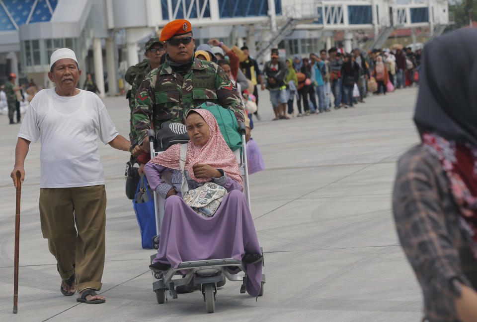 A woman is assisted on a luggage cart as her and hundreds of others line up to board an Air Force cargo plane at the Mutiara Sis Al-Jufri airport to evacuate the earthquake and tsunami-damaged city of Palu, Central Sulawesi Indonesia, Thursday, Oct. 4, 2018. Life is on hold for thousands living in tents and shelters in the Indonesian city hit by a powerful earthquake and tsunami, unsure when they'll be able to rebuild and spending hours each day often futilely trying to secure necessities such as fuel for generators. (AP Photo/Tatan Syuflana)