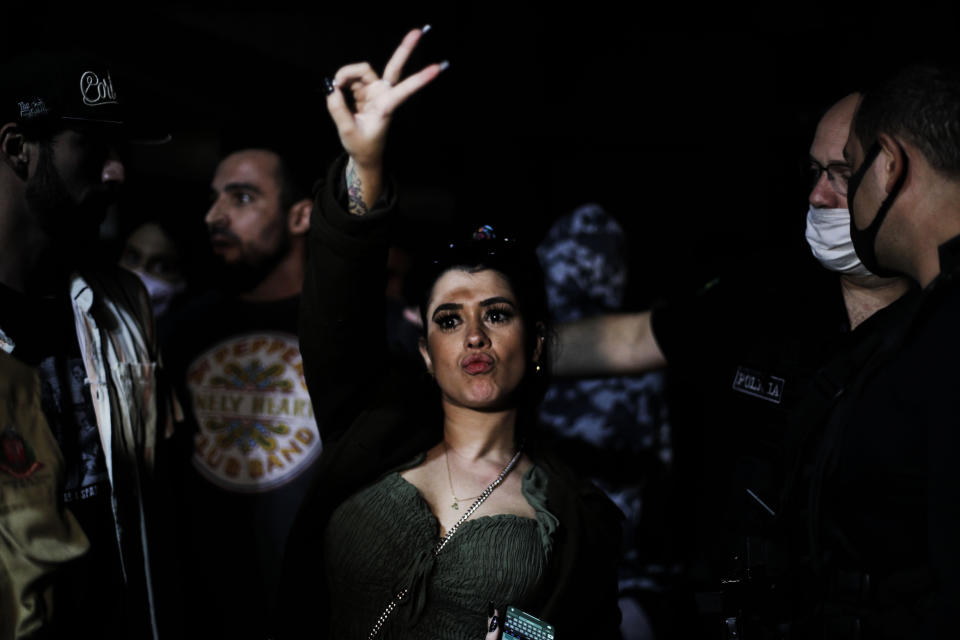 A woman flashes a V sign as police break up a social gathering during an operation against illegal and clandestine gatherings that authorities believe are partly responsible for fueling the spread of COVID-19, at a party hall in Sao Paulo, Brazil, early Saturday, April 17, 2021. Local leaders have found it hard to enforce restrictions while President Jair Bolsonaro is urging people to ignore them.(AP Photo/Marcelo Chello)