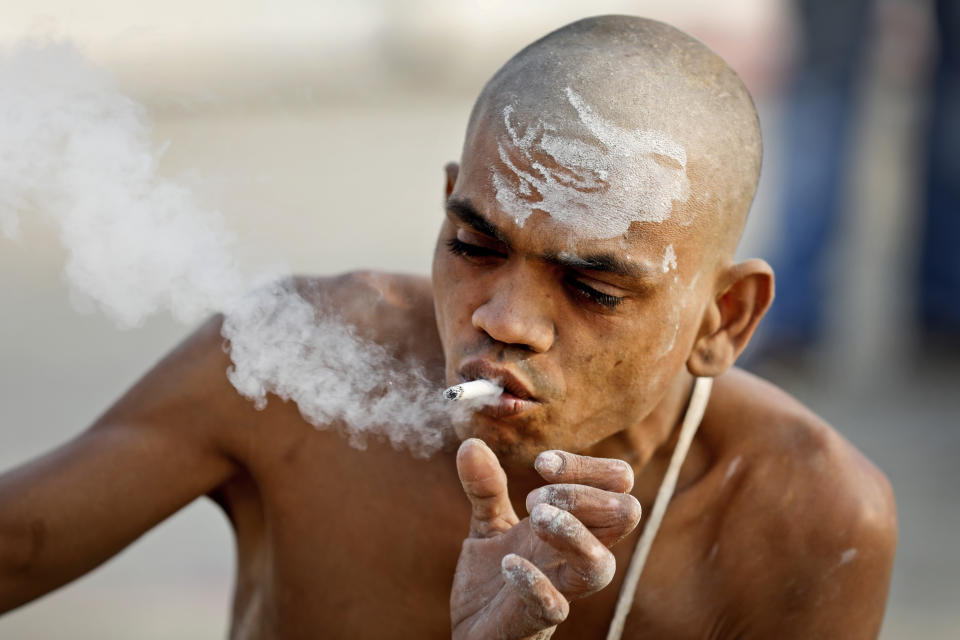 In this Jan. 27, 2019, photo, a Hindu holy man smokes a cigarette after a ritual for becoming Naga Sadhus or naked holy men at Sangam, the confluence of three holy rivers during the Kumbh Mela or pitcher festival in Prayagraj Uttar Pradesh state, India. At every Kumbh, including this year's, thousands of devotees were initiated into the reclusive sect of the Naga Sadhus, naked, ash-smeared cannabis-smoking Hindu warriors and onetime-armed defenders of the faith who for centuries have lived as ascetics in jungles and caves. (AP Photo/ Rajesh Kumar Singh)