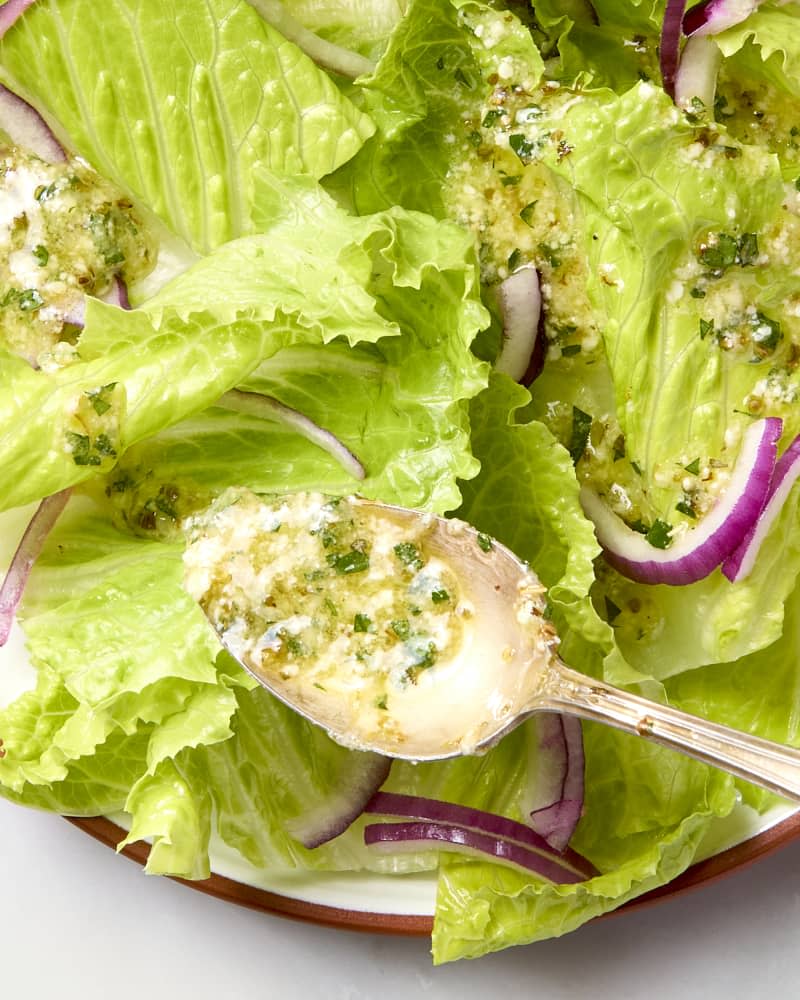 overhead shot of homemade italian dressing being spooned over a simple salad.