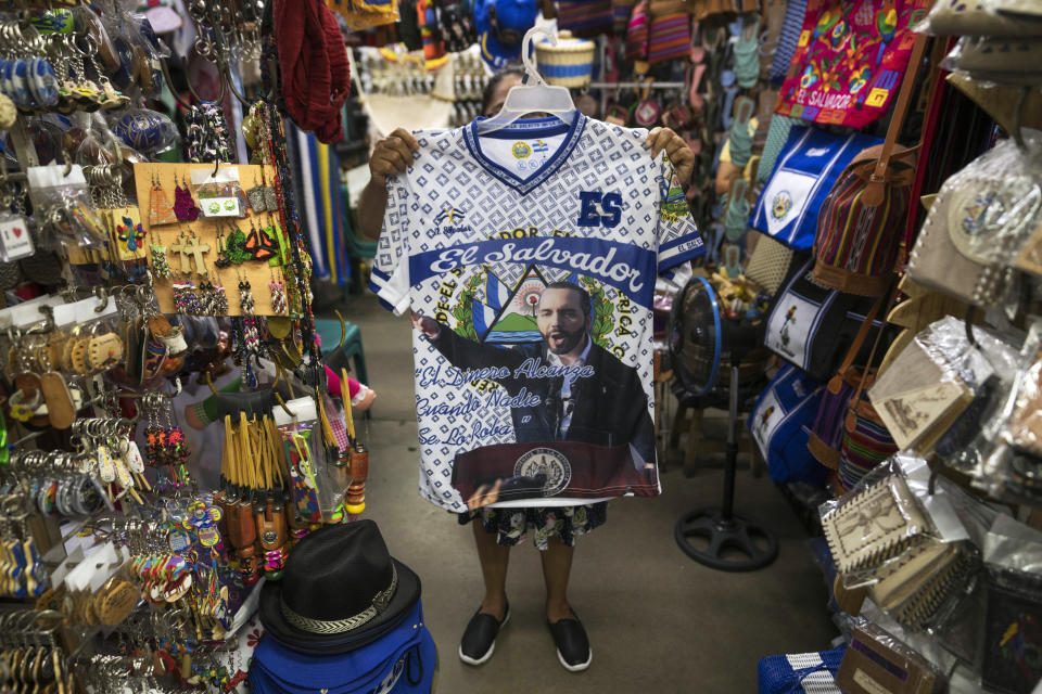 A vendor holds up a T-shirt with an image of El Salvador's President Nayib Bukele, at a craft market in the historic center of San Salvador, El Salvador, Saturday, Oct. 8, 2022. Bukele and his allies in congress launched a war against the gangs and suspended constitutional rights. Nearly seven months later, this “state of exception” is still widely popular. A CID Gallup survey puts Bukele’s approval ratings at 86%. (AP Photo/Moises Castillo)