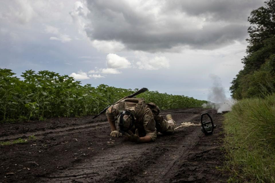 A soldier takes cover as he removes an anti tank mine by tying a rope around the detonator during a mine clearance exercise on July 11 2023, in Dnipropetrovsk region, Ukraine.