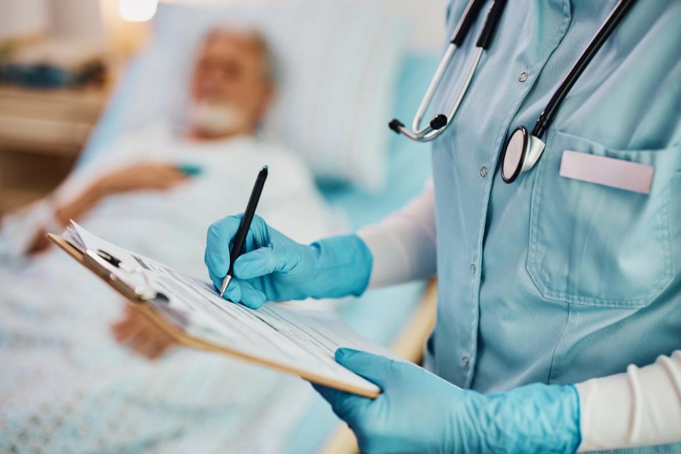 Close up of provider writing medical data of hospitalized patient while visiting him at intensive care unit.