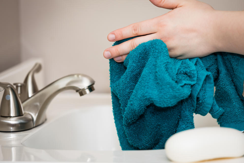 Drying off hands with a blue towel above the bathroom sink