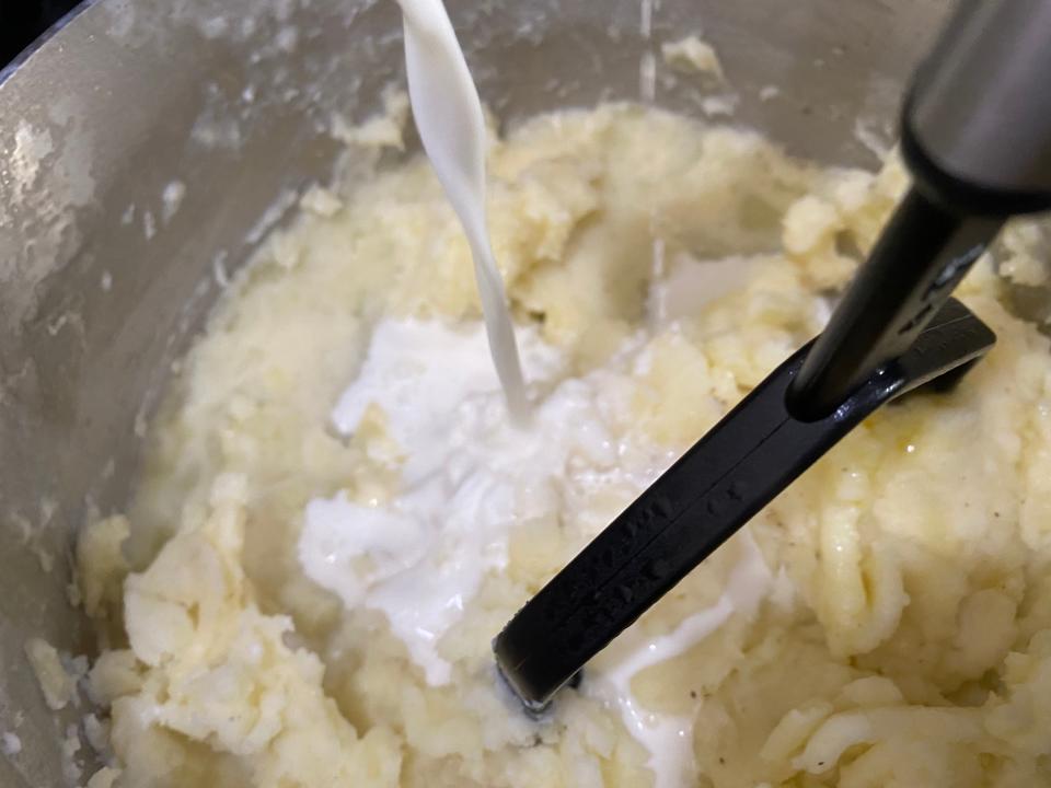 The cream mixture is poured into the bowl with mashed potatoes.