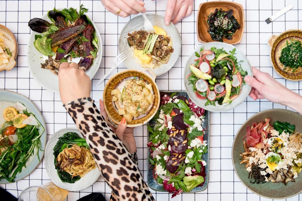 overhead photo of hands reaching for food dish with rice, greens, salads, and veggies