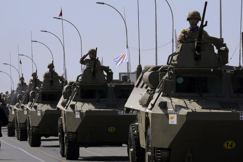 A female soldier on an armoured vehicle, center, salutes during a military parade marking the 62nd anniversary of Cyprus' independence from British colonial rule, in Nicosia, Cyprus, Saturday, Oct. 1, 2022. Cyprus gained independence from Britain in 1960 but was split along ethnic lines 14 years later when Turkey invaded following a coup aimed at uniting the island with Greece. (AP Photo/Petros Karadjias)